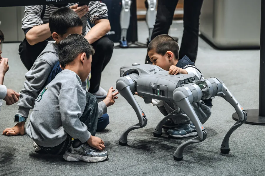 Kids watching a four-legged robot dog walk across the floor