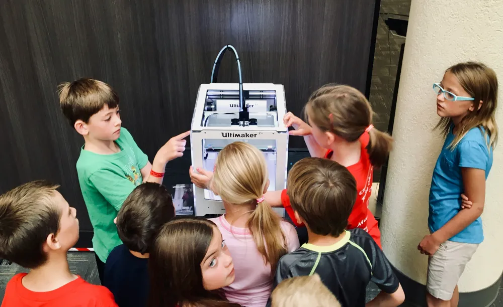 Children gathered around a 3D printer in a maker lab