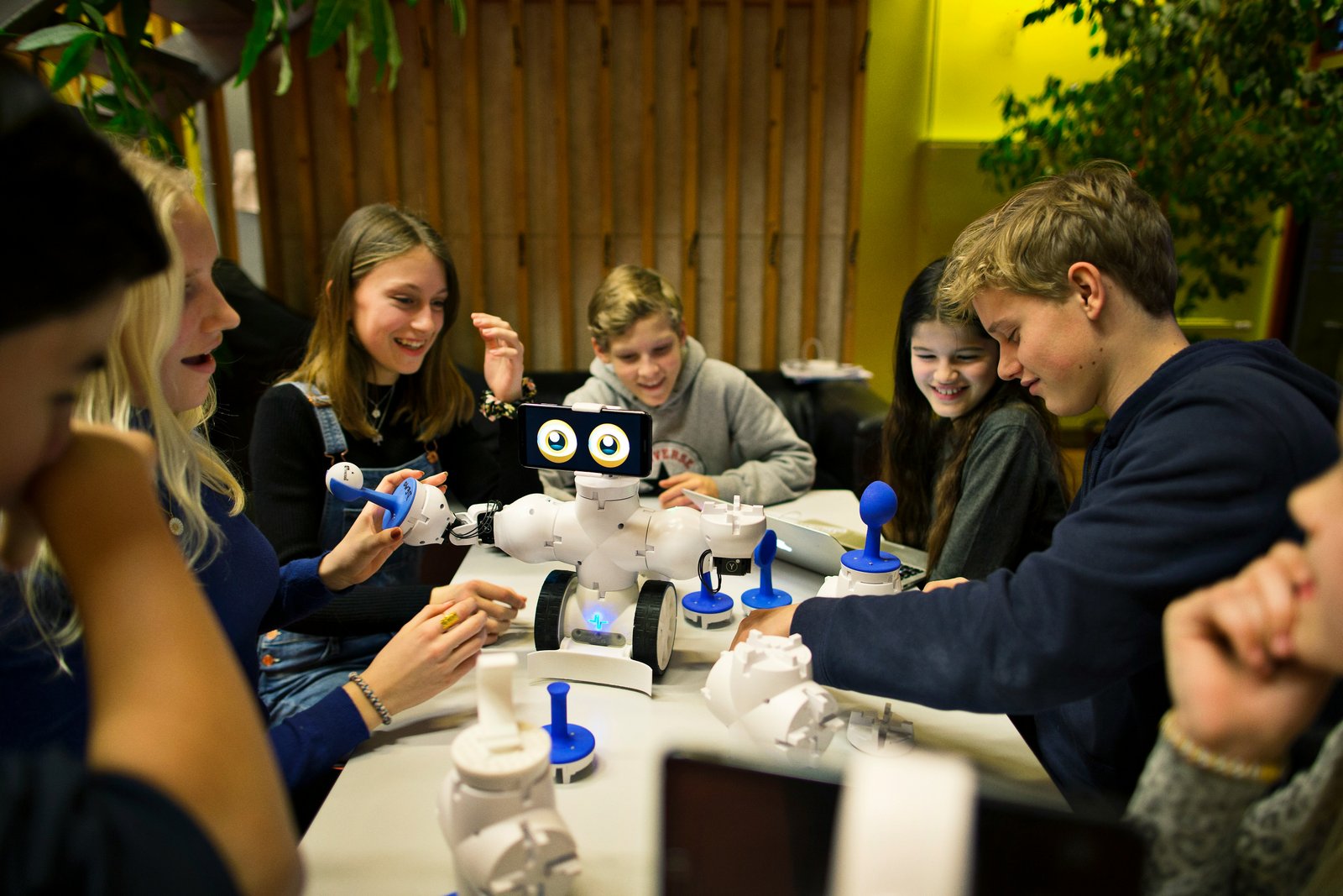 Young campers and teens building small white robots together at a table