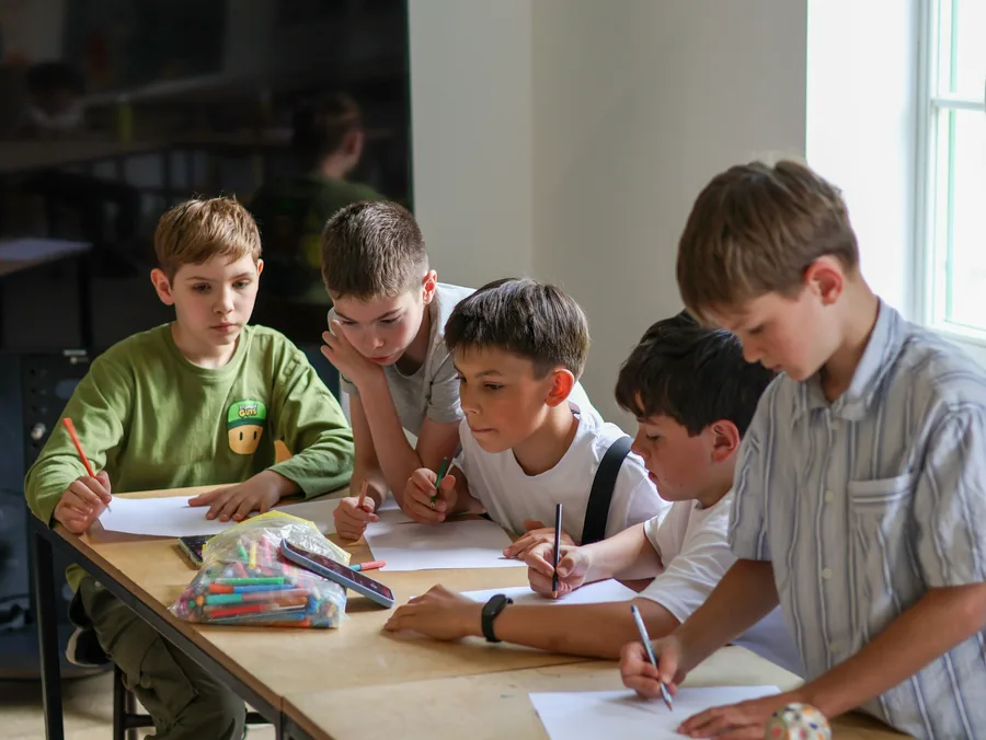 Four kids drawing robot ideas on paper at a shared table